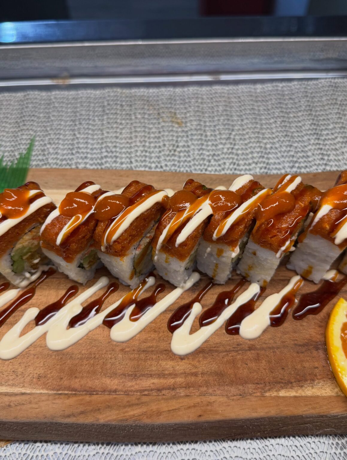 Sushi roll with spicy topping and drizzled sauces on wooden board