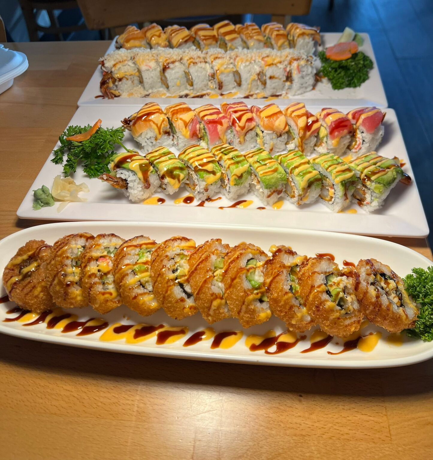 Three platters of assorted sushi rolls with colorful sauces