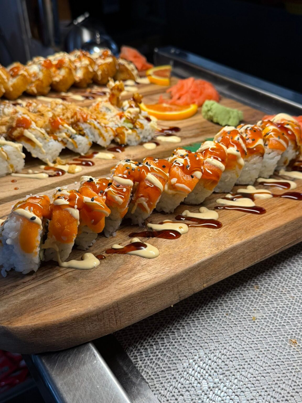 Assorted sushi rolls drizzled with sauce on wooden board
